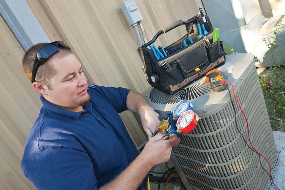 Man performing a heat pump maintenance test with tools resting on unit