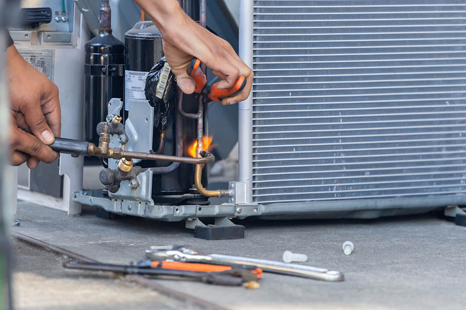 Close-up of an HVAC technician repairman on the floor fixing heat pump system with welding tools